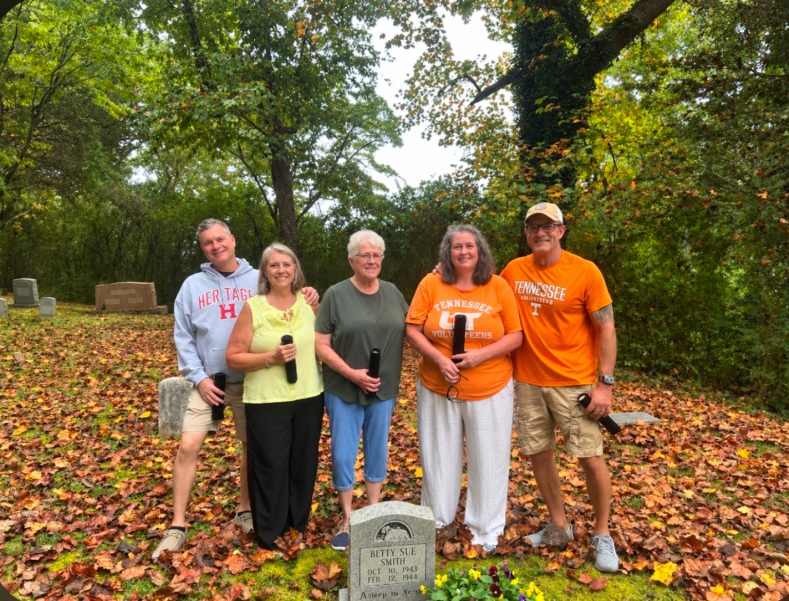 Five adult siblings standing together at a cemetery graveside